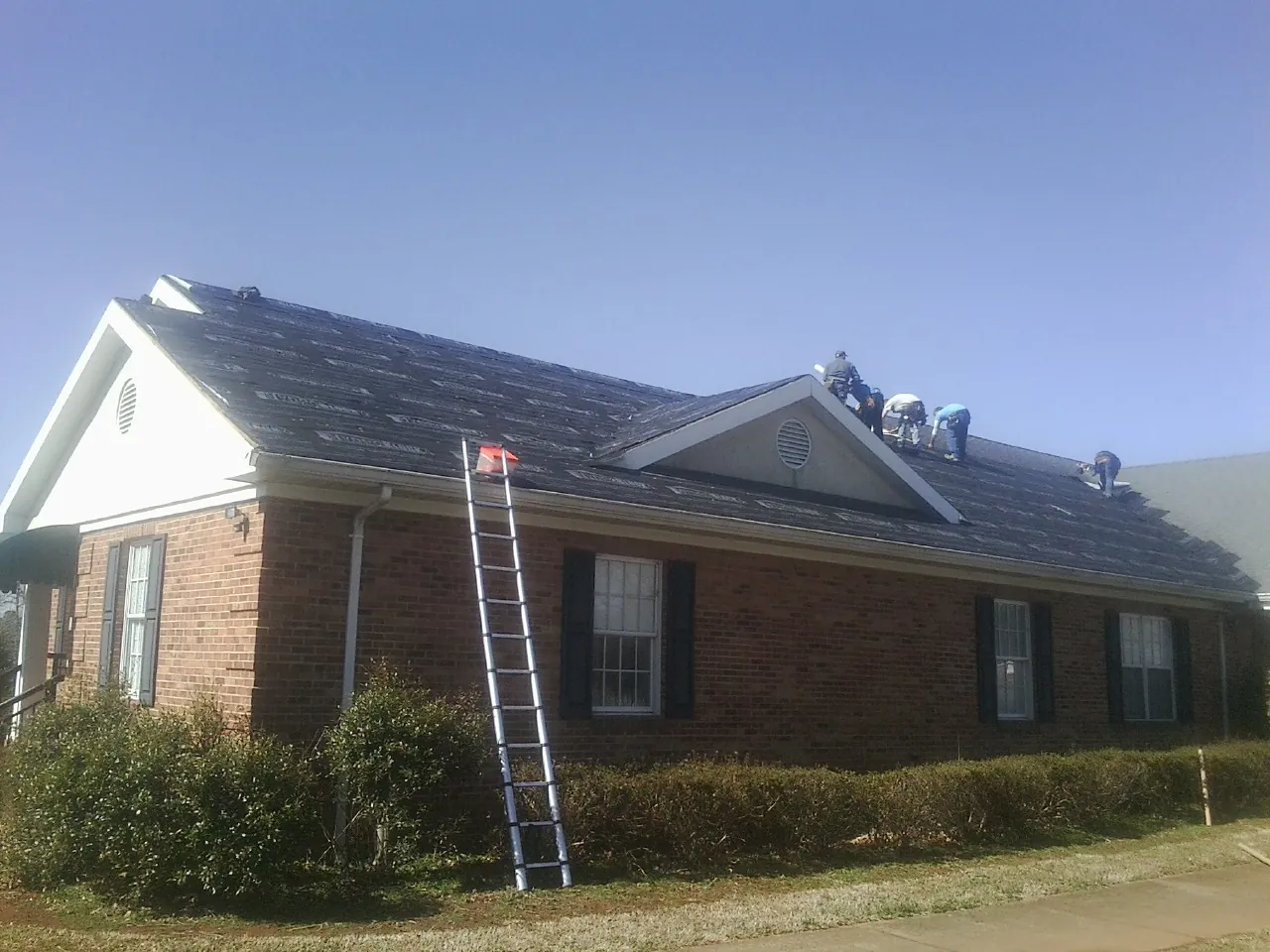 Crew tearing shingles off a brick ranch roof with a ladder set — Metal Roof Repair work by our crew in Golden